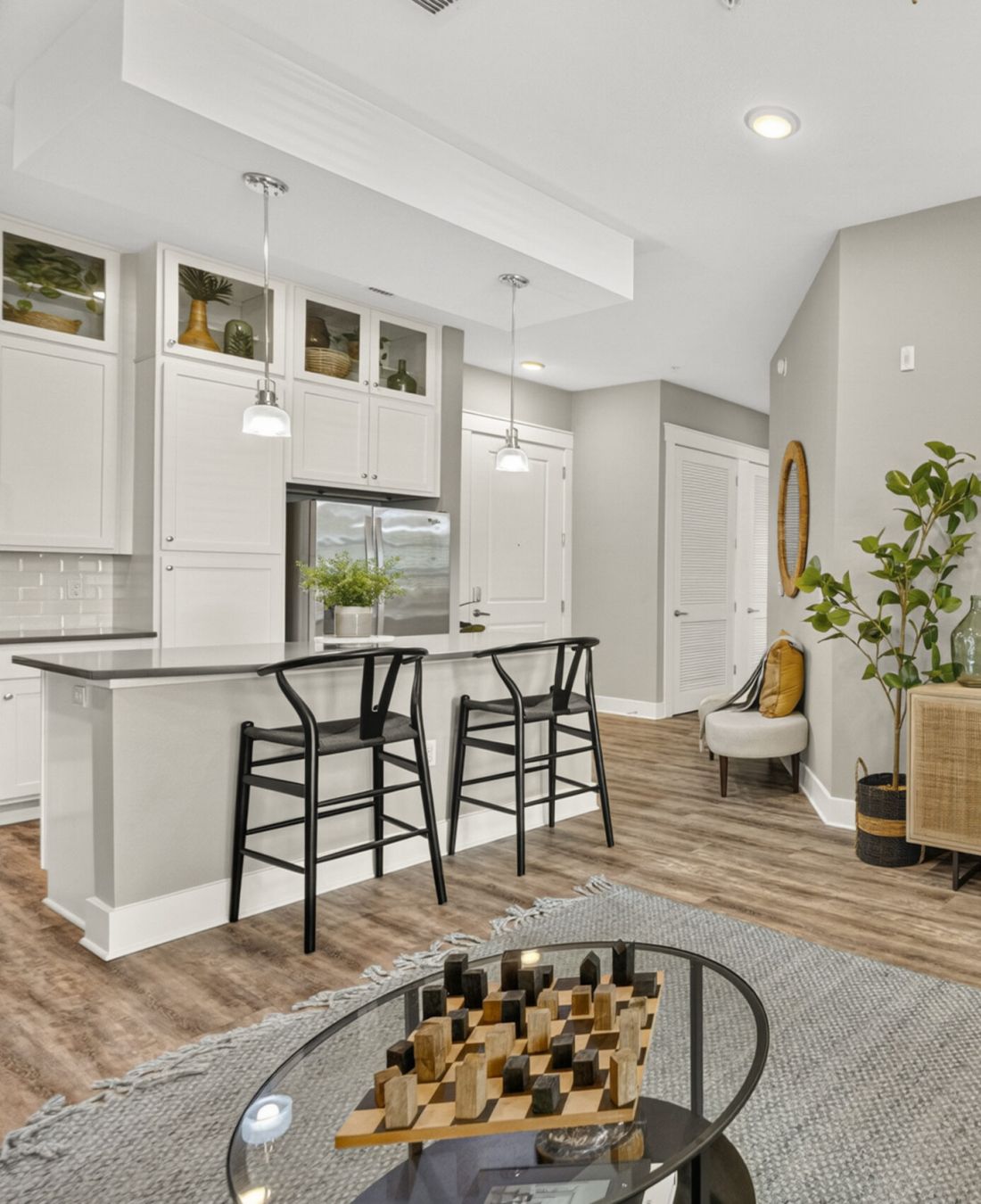 Novus Modern living room with neutral decor, a round coffee table, and an open kitchen with black barstools and white cabinets.